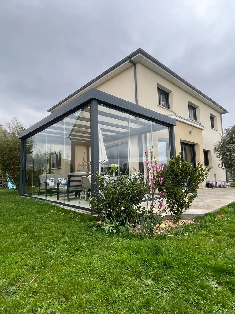 Véranda verre toit anthracite sur maison beige, salon gris et magnolia en fleurs