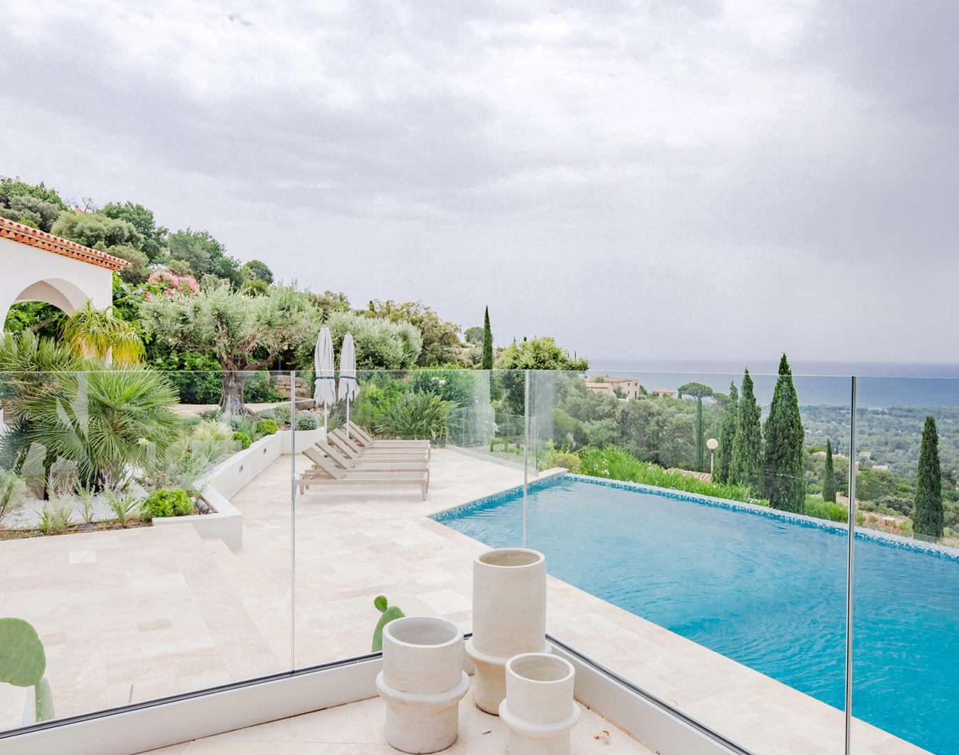 Terrasse piscine débordement, garde-corps verre, transats et vue mer collines
