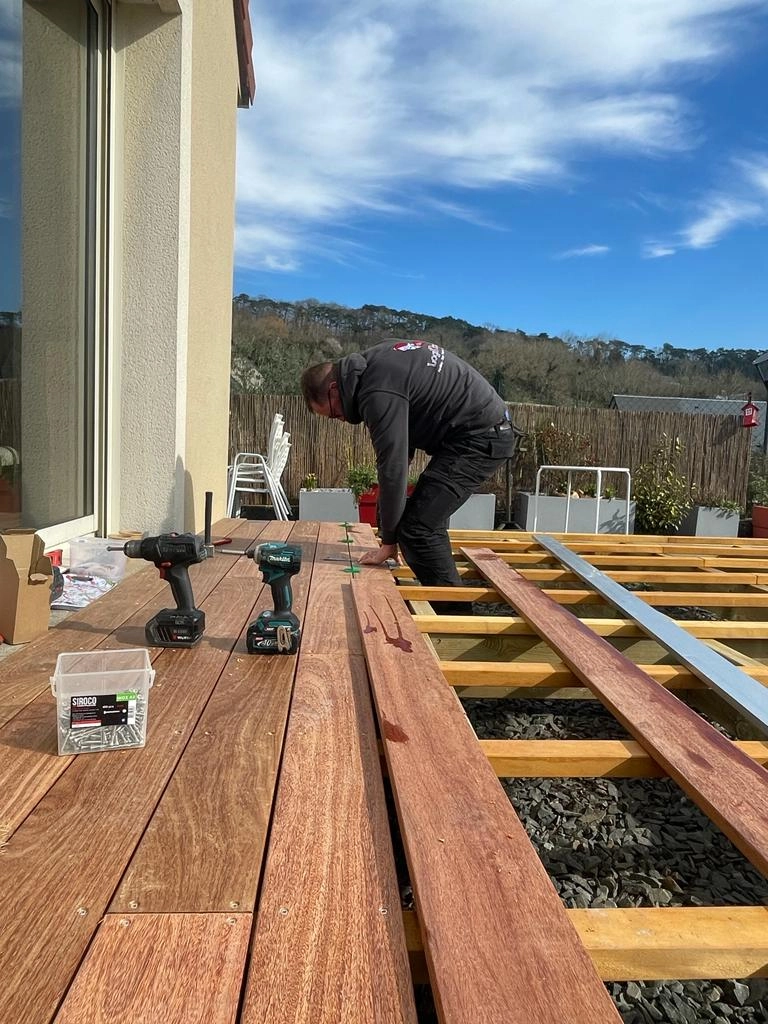 Artisan Logikinov posant lames terrasse bois sur lambourdes, visseuses au premier plan