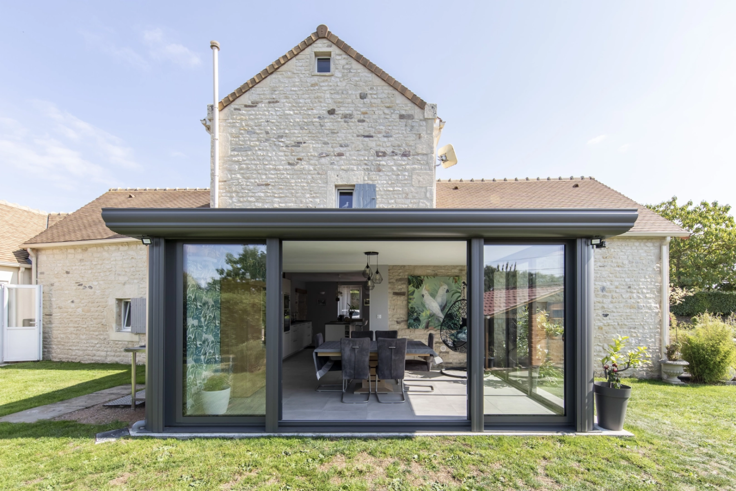 Extension anthracite baies coulissantes ouvertes sur salle à manger, maison pierre ancienne