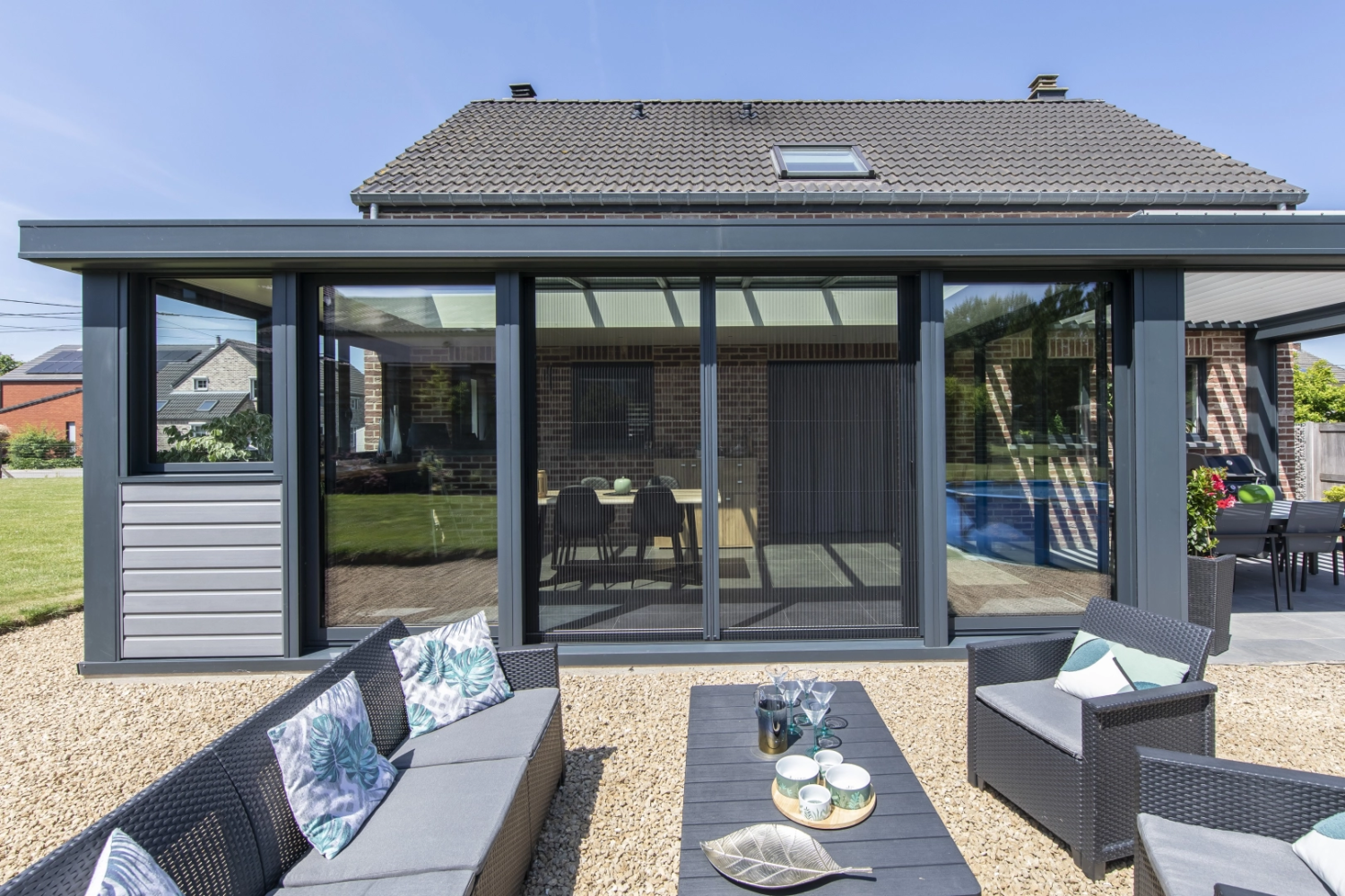 Véranda anthracite baies coulissantes, salon résine noir sur gravier, maison briques