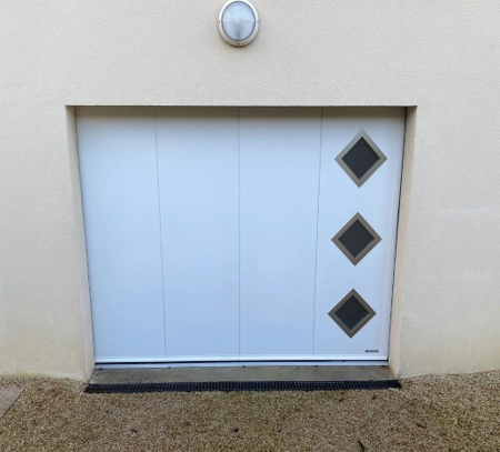 Porte garage blanche rainures verticales, trois hublots carrés en losange à droite