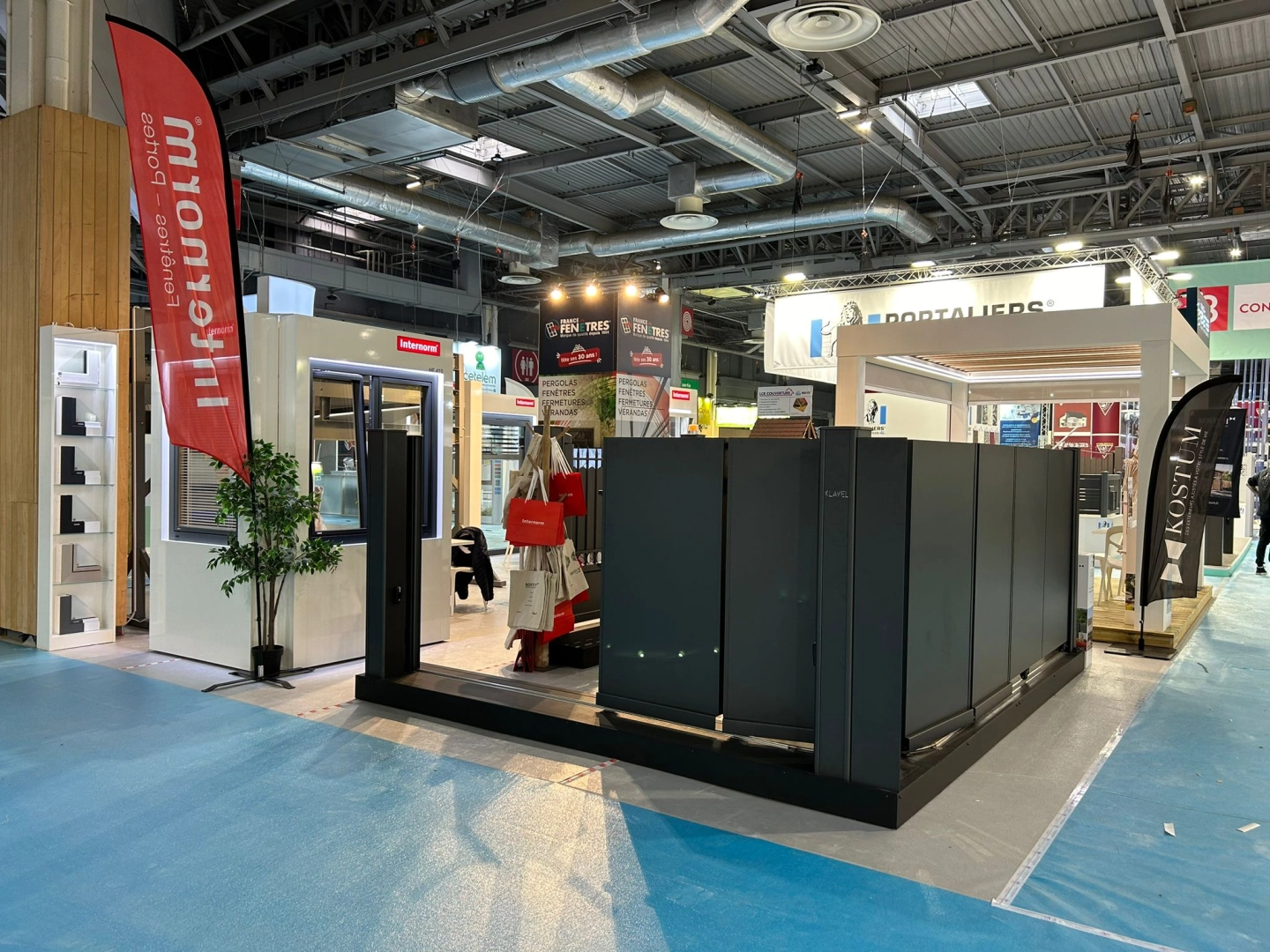 Stand salon : portail gris, pergola blanche, drapeaux Internorm et Kostum