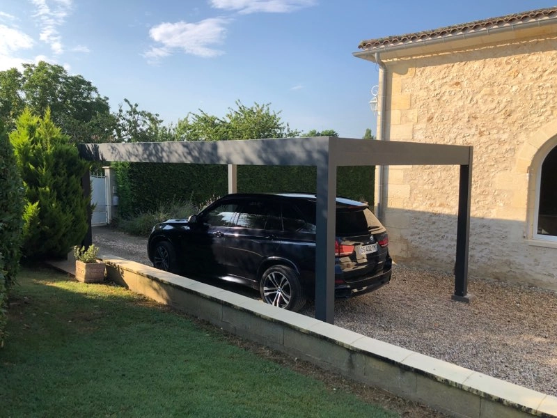 SUV noir sous carport anthracite devant maison pierre claire et jardin