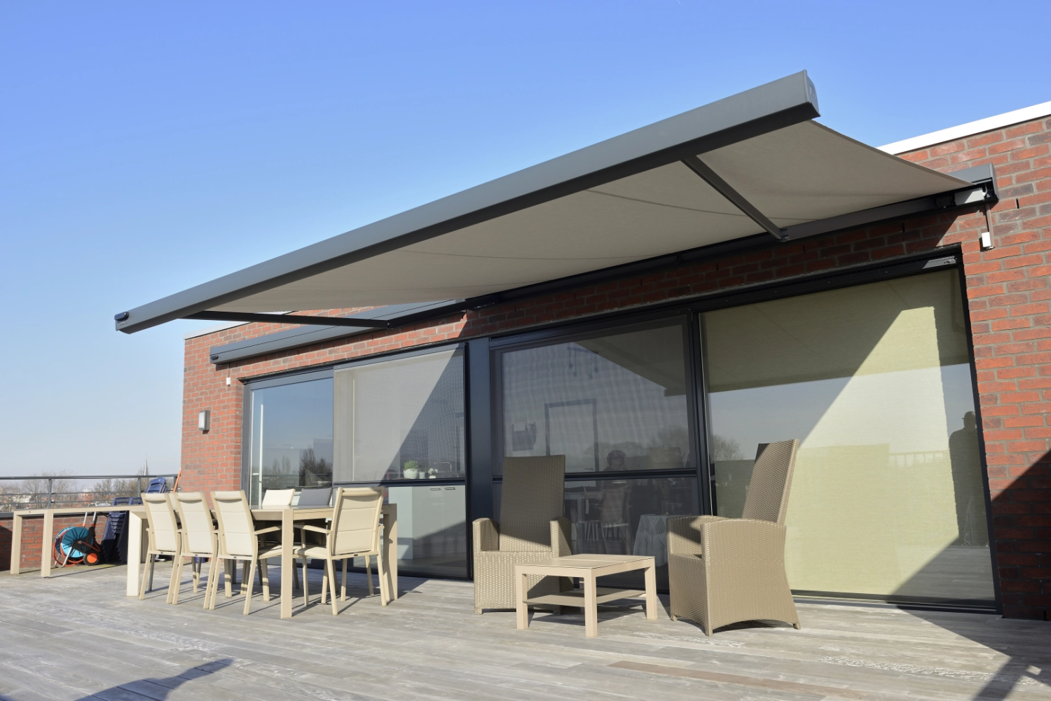 Store banne beige sur terrasse bois, table à manger et salon résine devant briques