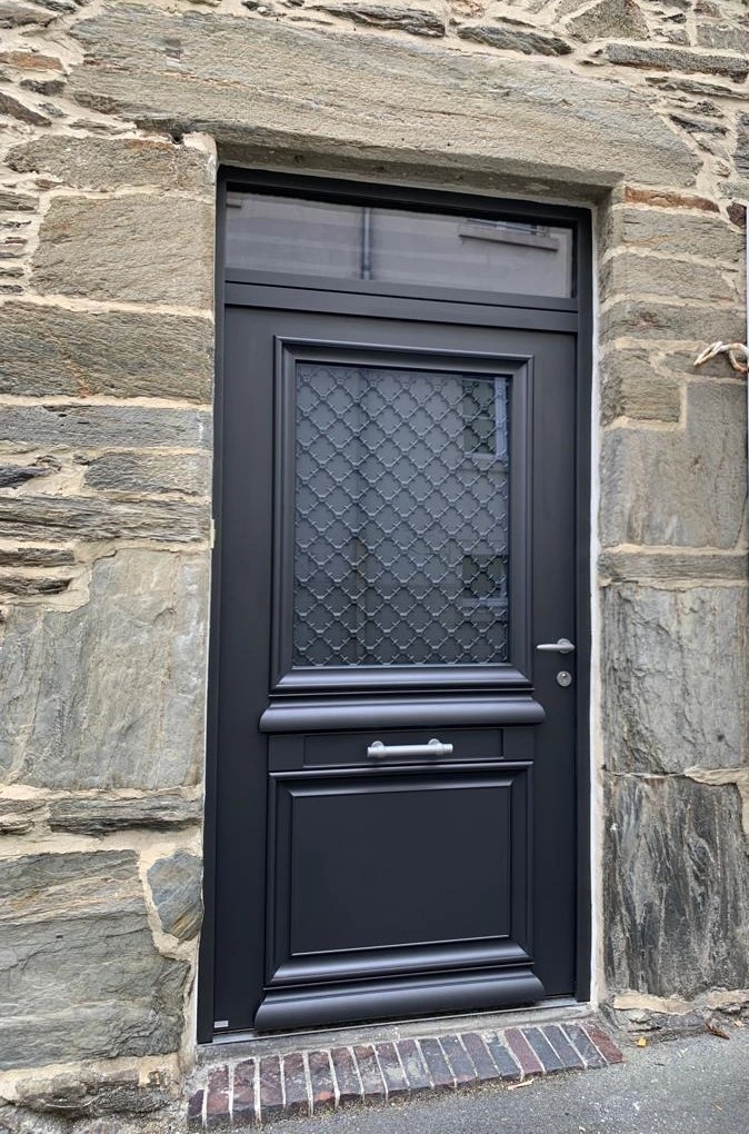 Porte gris anthracite grille losanges et imposte sur mur pierres, seuil briques
