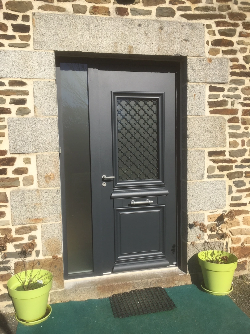 Porte anthracite à grille décorative et vitrage latéral sur pierre avec pots vert pomme