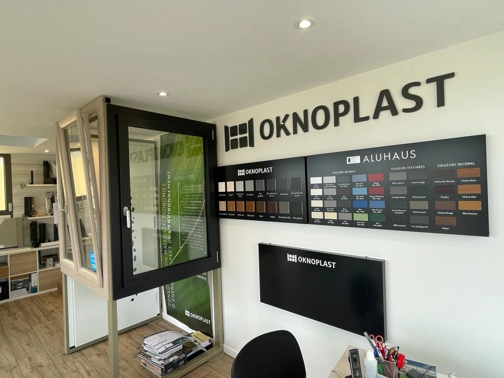 Showroom fenêtres noires et bois, nuanciers et Logo Oknoplast au mur