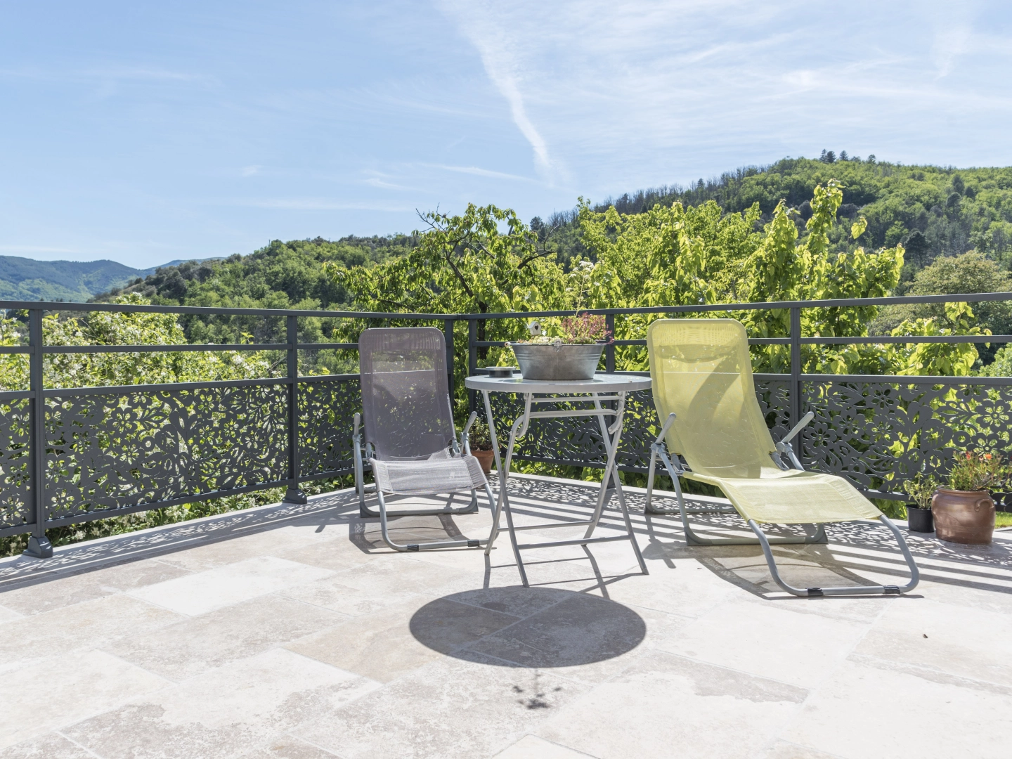 Terrasse dalles claires, garde-corps anthracite motifs floraux, transats face collines