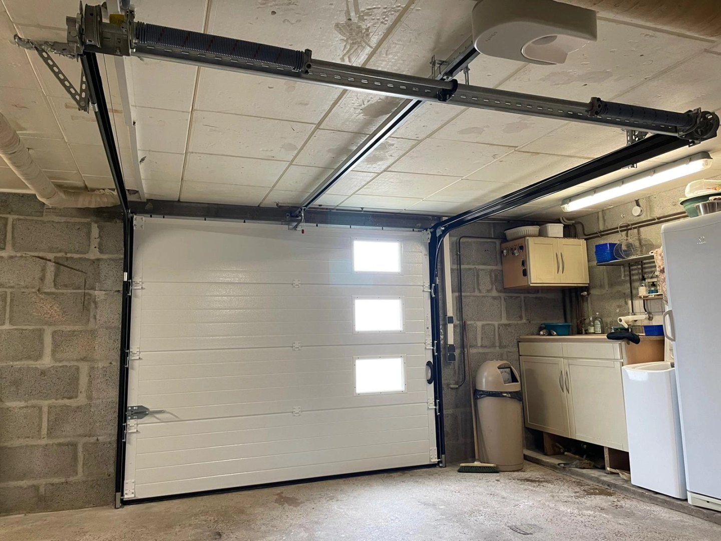 Garage porte sectionnelle blanche trois hublots, rails plafond et armoire utilitaire