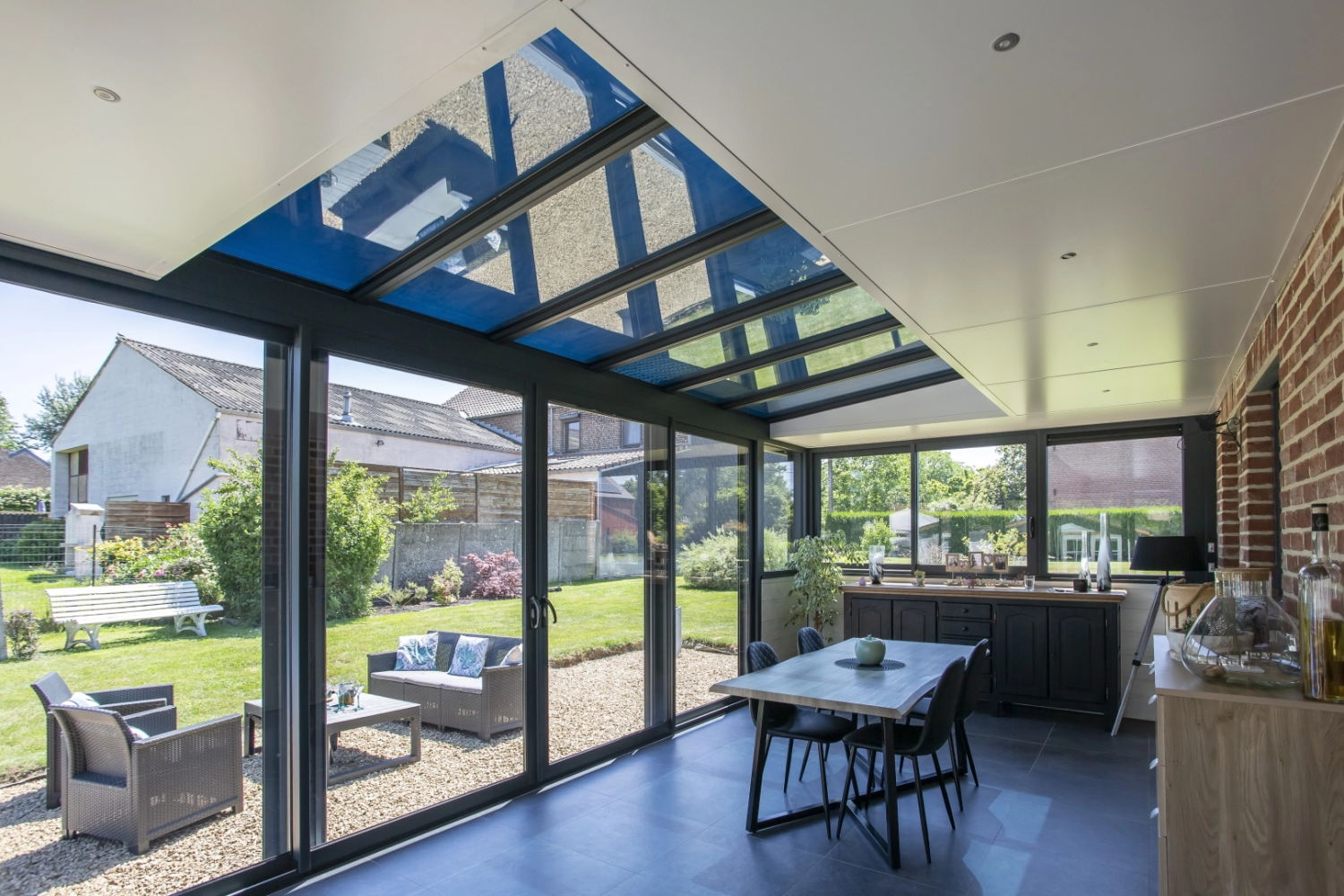 Véranda baies coulissantes noires toit vitré, terrasse jardin et salon extérieur