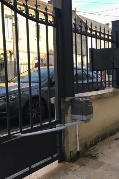 Motorisation Somfy sur portail noir à barreaudage, bras articulé fixé sur pilier pierre