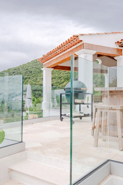 Garde-corps entièrement vitré sur terrasse avec vue colline verte, barbecue et bar en bois