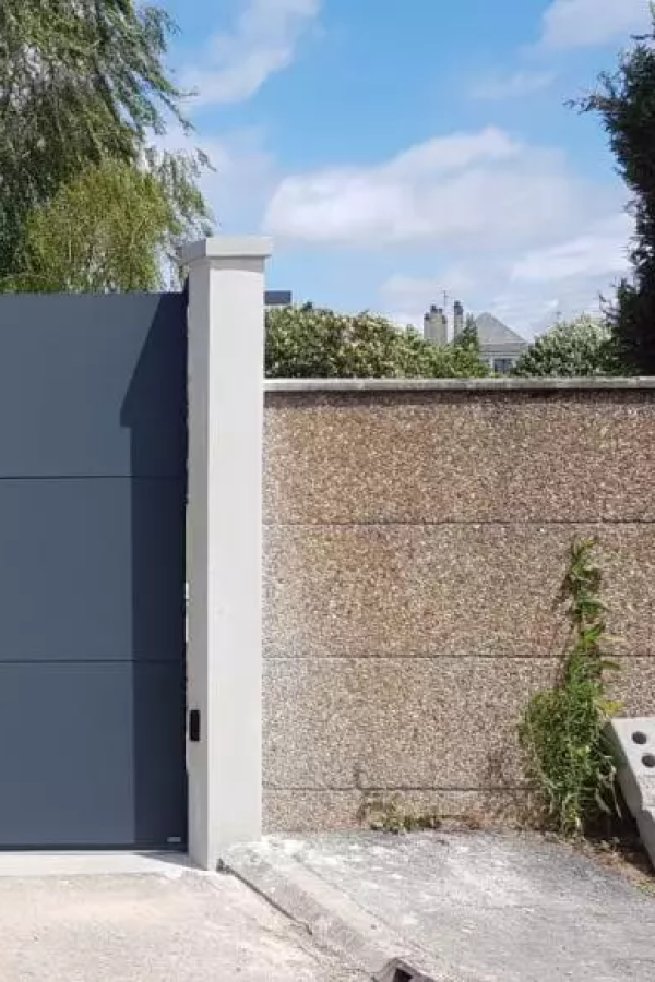 Portail battant aluminium gris anthracite devant pilier beige et mur crépi grainé, ciel bleu