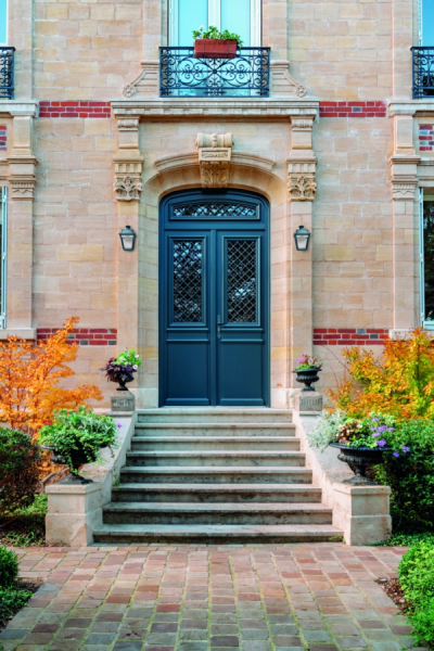 Porte double bleu nuit à grille fer forgé dans encadrement pierre, escalier et massif fleuri