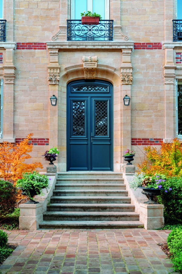 Porte double bleu nuit à grille fer forgé dans encadrement pierre, escalier et massif fleuri
