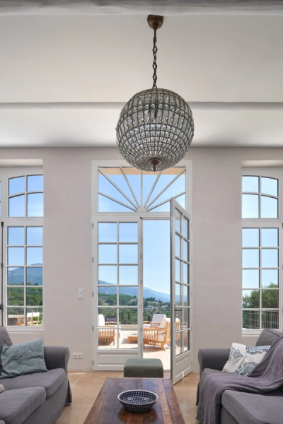 Salon porte-fenêtre blanche imposte rayonnante ouverte, vue montagnes et sofas gris