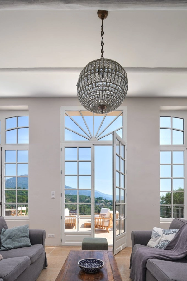 Salon porte-fenêtre blanche imposte rayonnante ouverte, vue montagnes et sofas gris