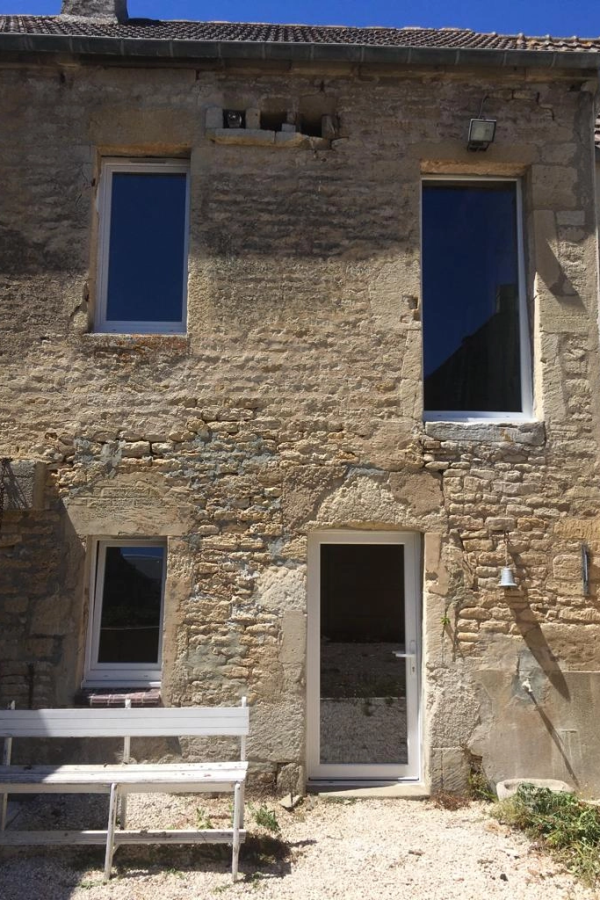 Maison pierre avec fenêtres et porte PVC blanches neuves, banc blanc sur gravier