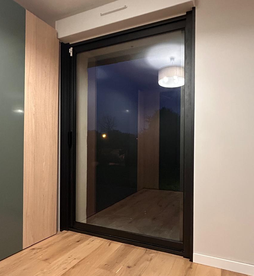 Pièce au parquet clair avec porte-fenêtre alu noir et placard intégré vert sauge