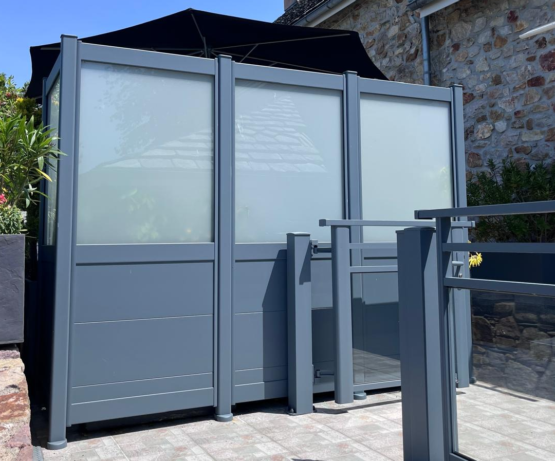 Brise-vue alu anthracite à panneaux bas pleins et verre dépoli, terrasse dalles devant maison pierre