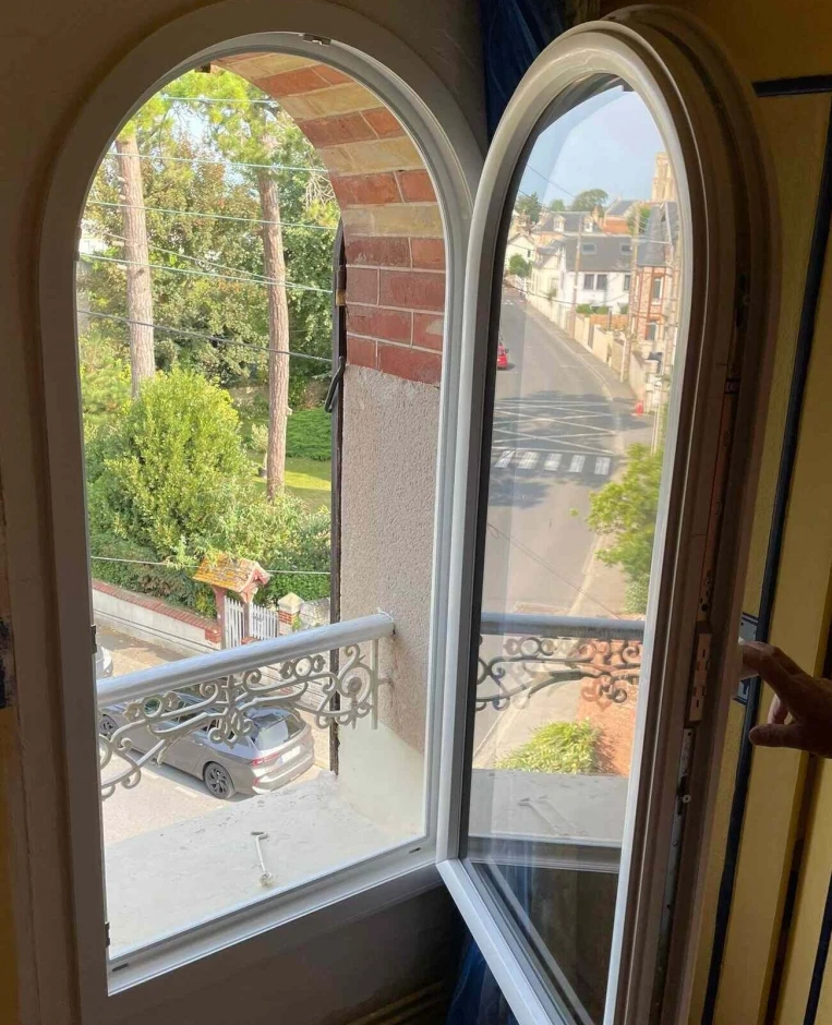 Fenêtre cintrée blanche ouverte, garde-corps fer forgé, vue rue et passage piéton