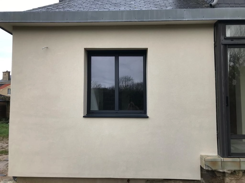 Fenêtre anthracite deux vantaux sur enduit beige clair, gouttière zinc et baie voisine