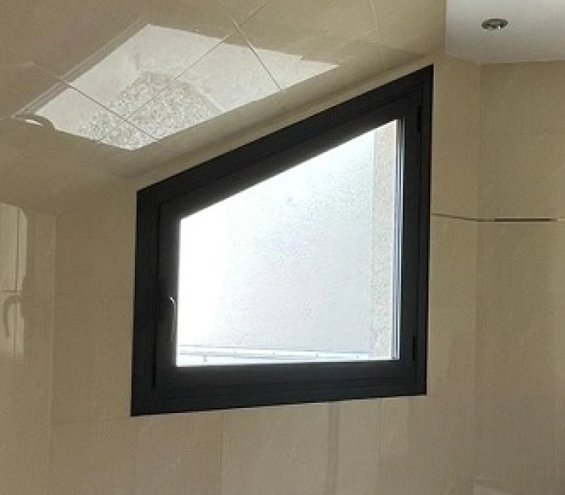 Fenêtre inclinée cadre gris foncé, vitrage dépoli dans salle de bains carrelée beige