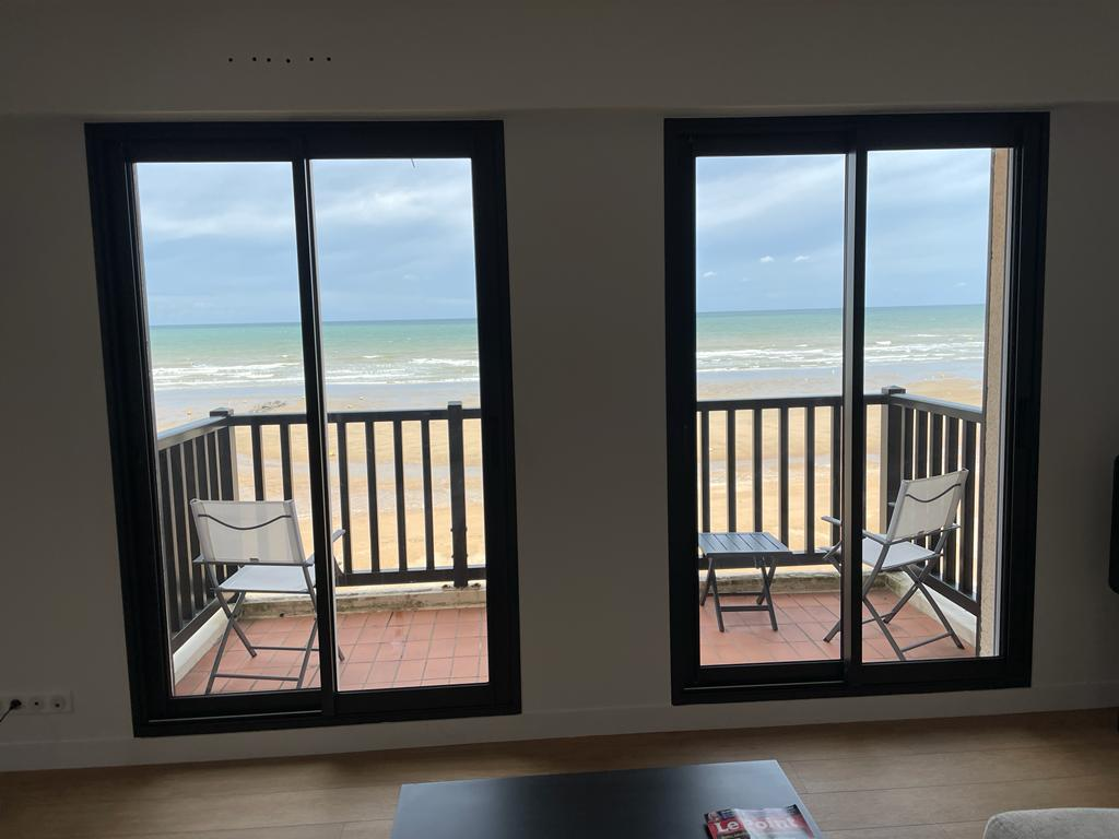 Vue intérieure sur balcon et plage à travers deux baies coulissantes alu noir