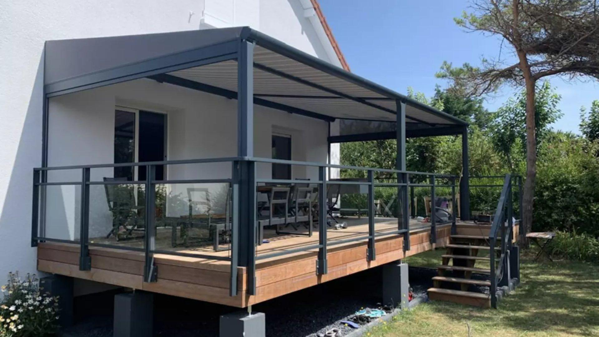 Pergola gris anthracite sur terrasse bois surélevée, garde-corps verre et fauteuils gris