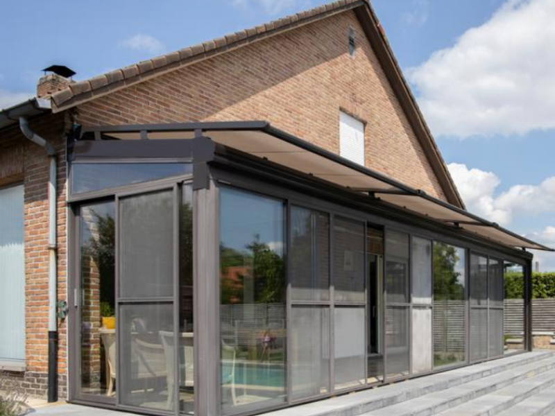 Véranda alu anthracite sur brique, store toiture beige et écrans gris sur vitrages