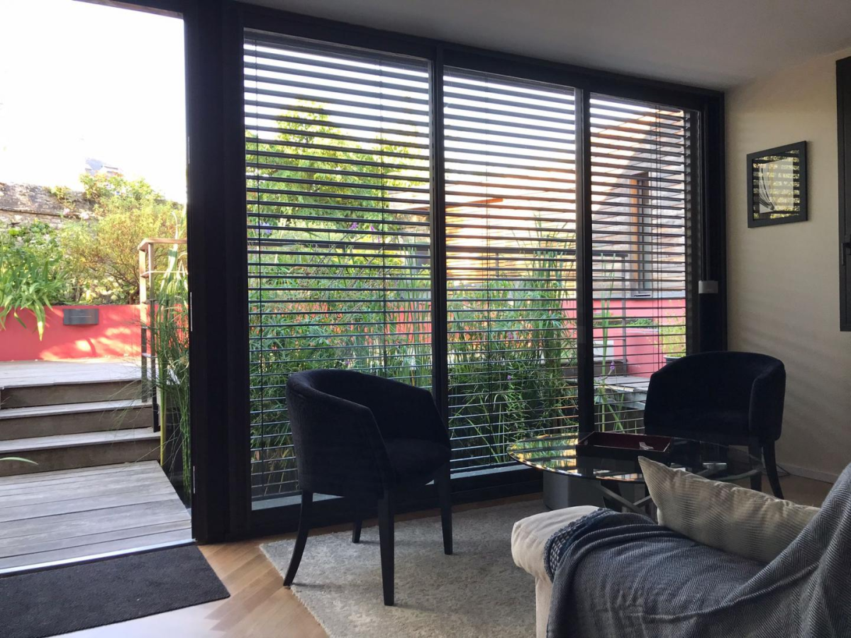 Salon, BSO anthracite sur baie vitrée, porte ouverte sur terrasse bois ensoleillée