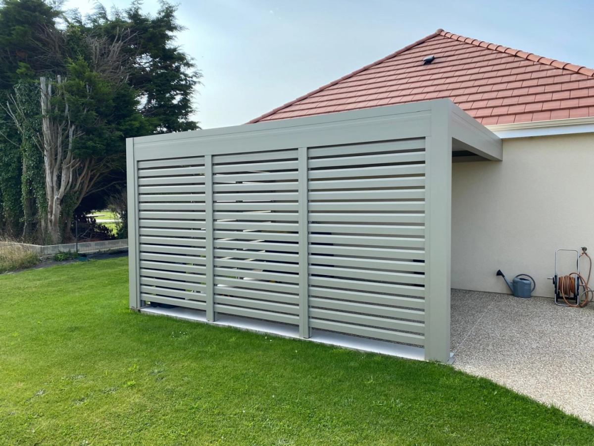 Carport anthracite adosse abritant une voiture sur graviers devant une facade beige