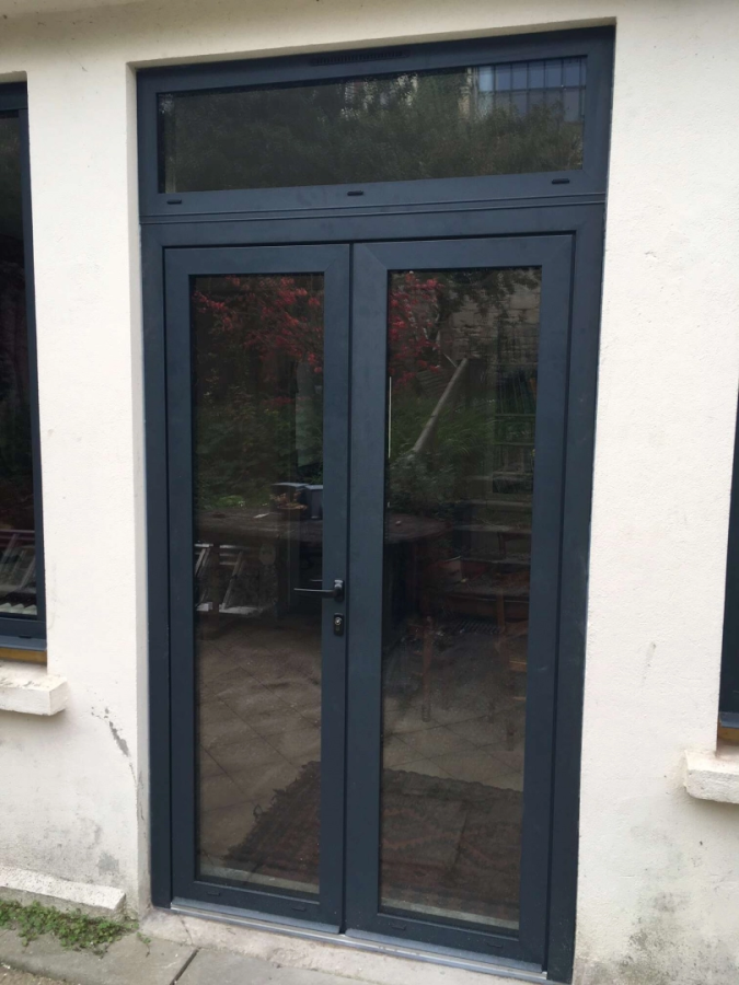 Porte-fenêtre double vitrée gris anthracite avec imposte, reflets jardin sur enduit clair