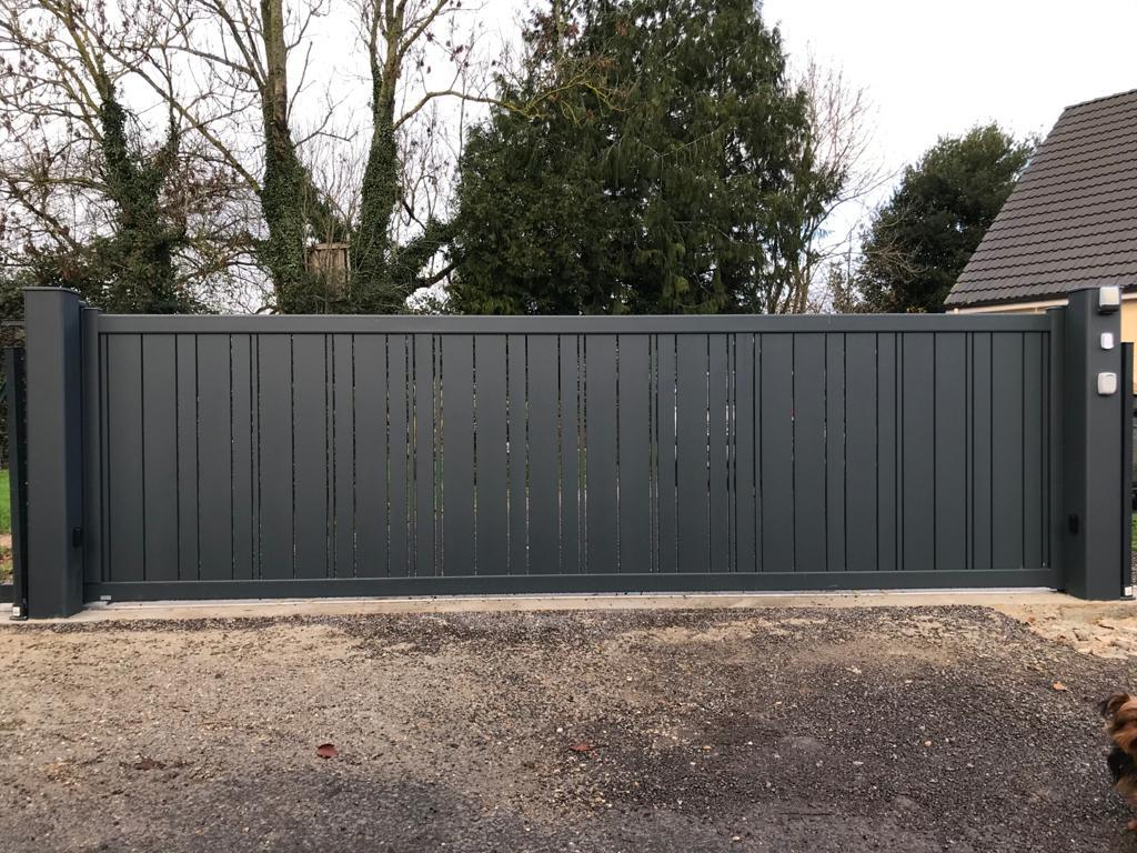 Portail coulissant anthracite lames verticales alternées entre piliers gris sur gravier