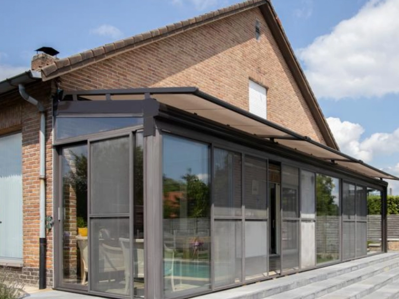 Véranda alu anthracite sur brique, moustiquaires, store toiture beige, terrasse pierre