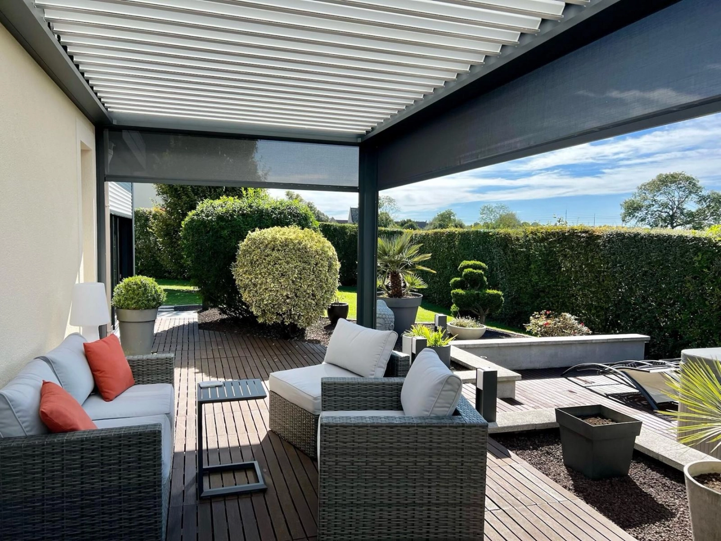 Pergola bioclimatique gris anthracite, lames blanches et stores zip sur salon de jardin