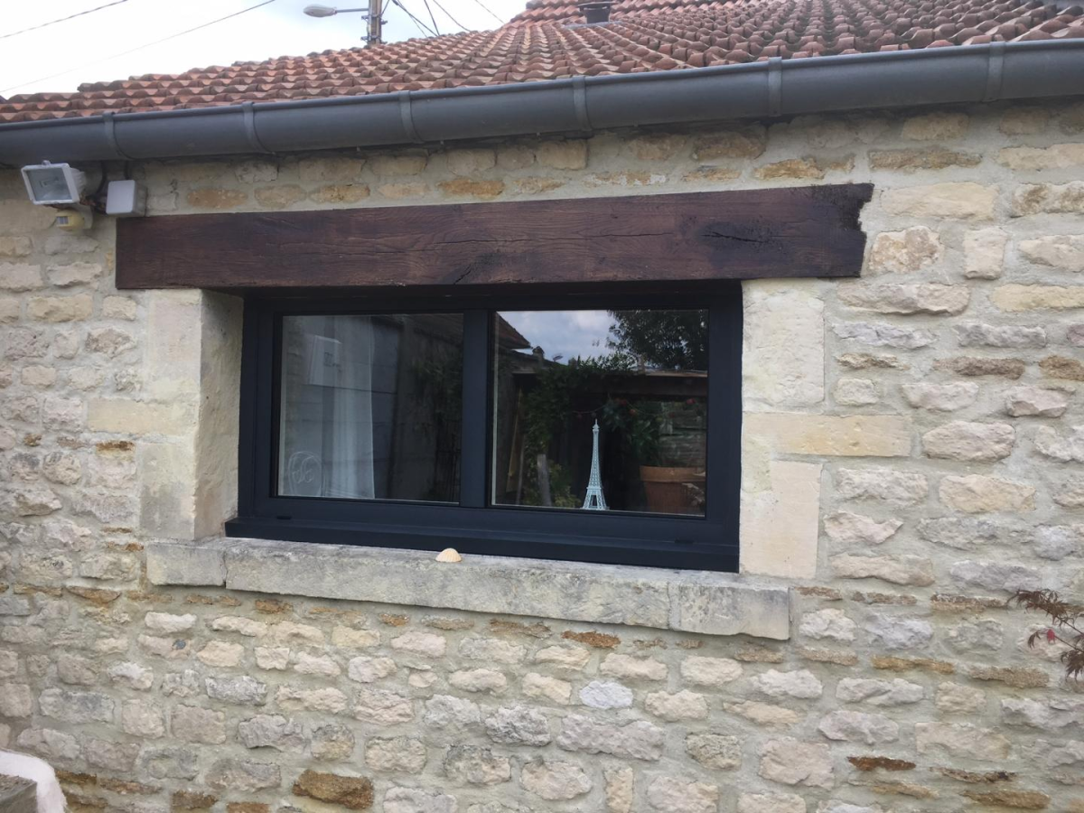 Fenêtre coulissante horizontale anthracite dans mur pierre, linteau bois et jardin