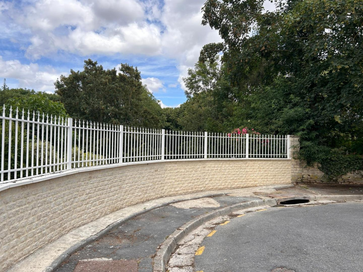 Cloture blanche barreaux pointus sur muret pierre beige courbe le long d une route