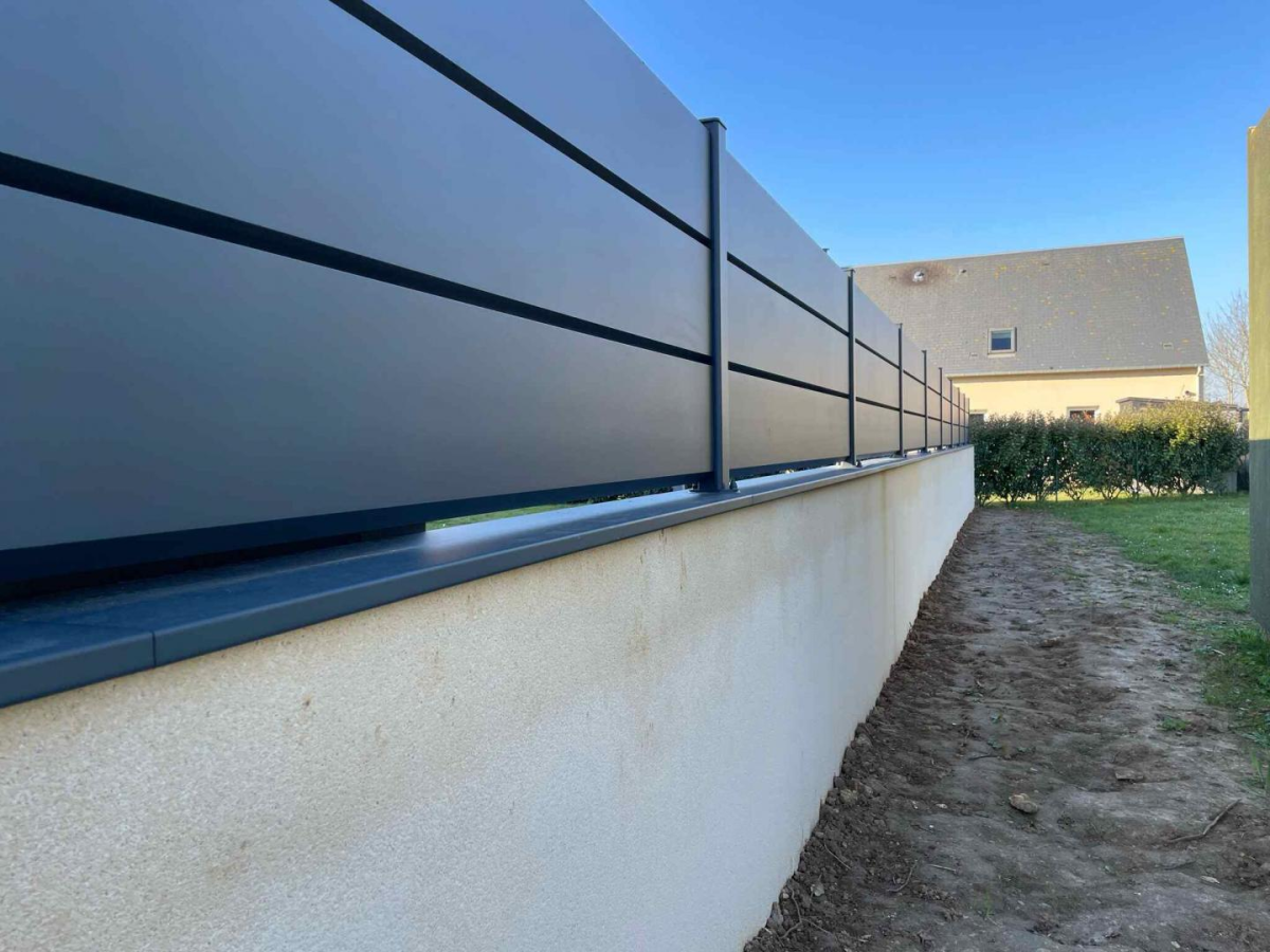 Cloture semi-ajourée anthracite lames horizontales sur muret beige le long d une pelouse