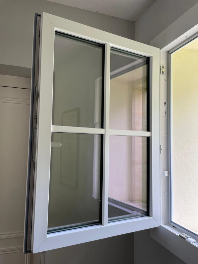 Fenêtre PVC blanche battante grande ouverte, quatre carreaux et mécanisme visible