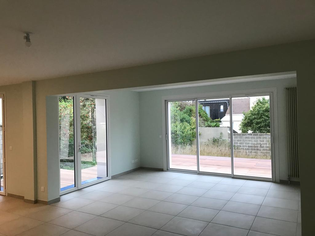 Pièce vide carrelée gris, baie vitrée blanche trois vantaux, vue terrasse bois