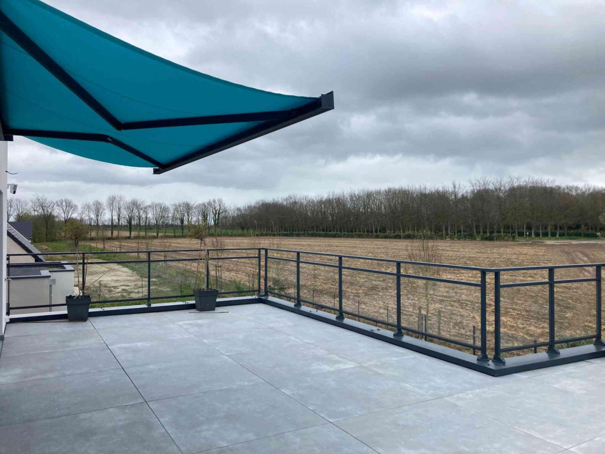 Terrasse carrelée avec store banne turquoise et garde-corps noir, vue campagne