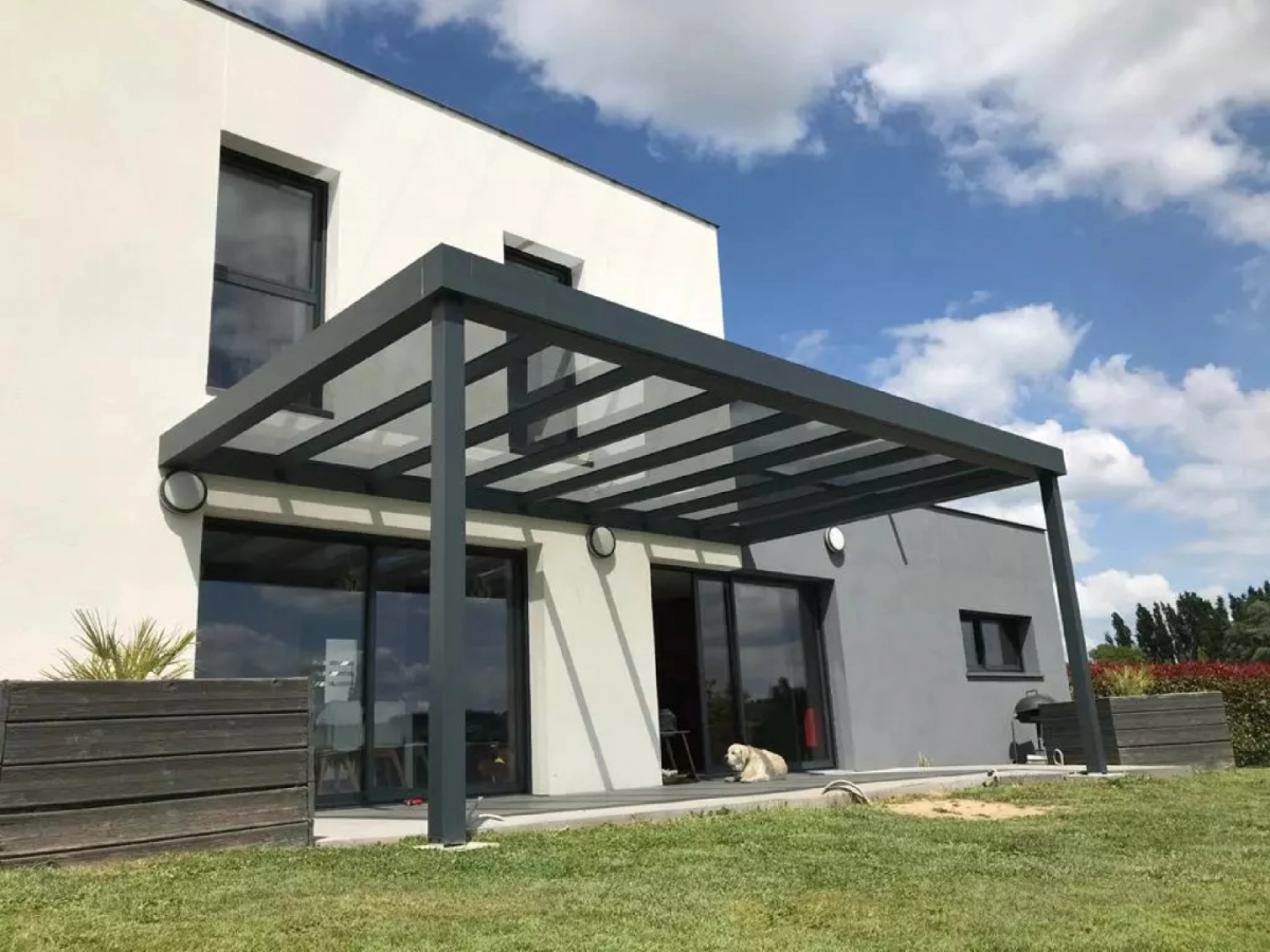 Pergola alu anthracite toit transparent sur terrasse bois devant maison blanche et grise