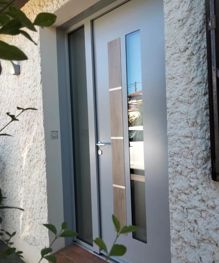 Porte d'entrée grise, vitrage latéral, bandeau aspect bois et rails alu, crépi blanc
