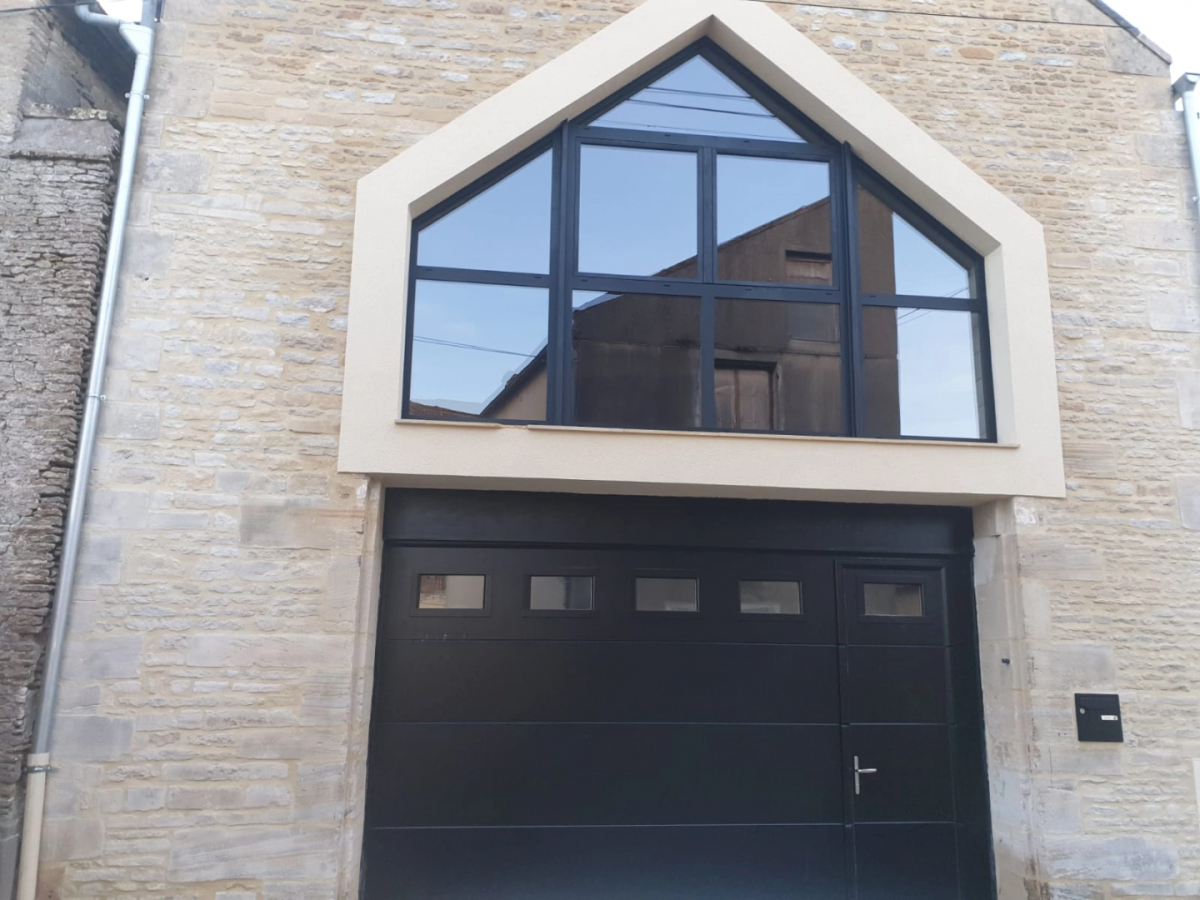 Porte garage sectionnelle noire avec portillon, grande fenêtre de pignon noire sur pierre