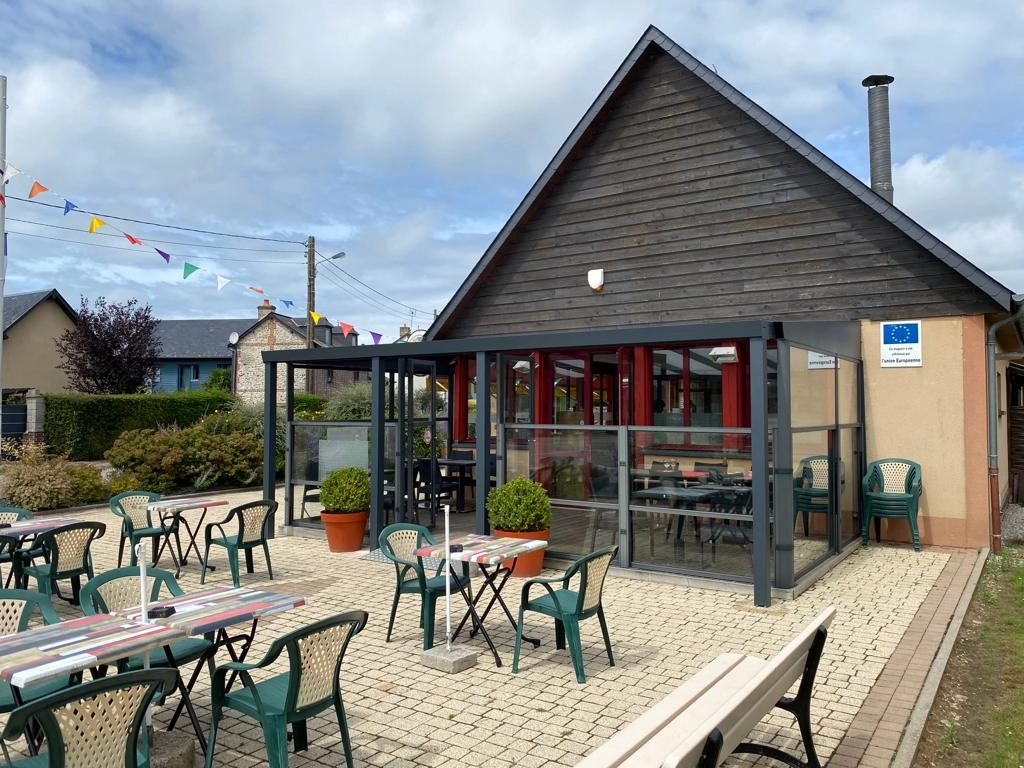 Veranda grise devant une terrasse de cafe avec chaises vertes et pignon bois sombre