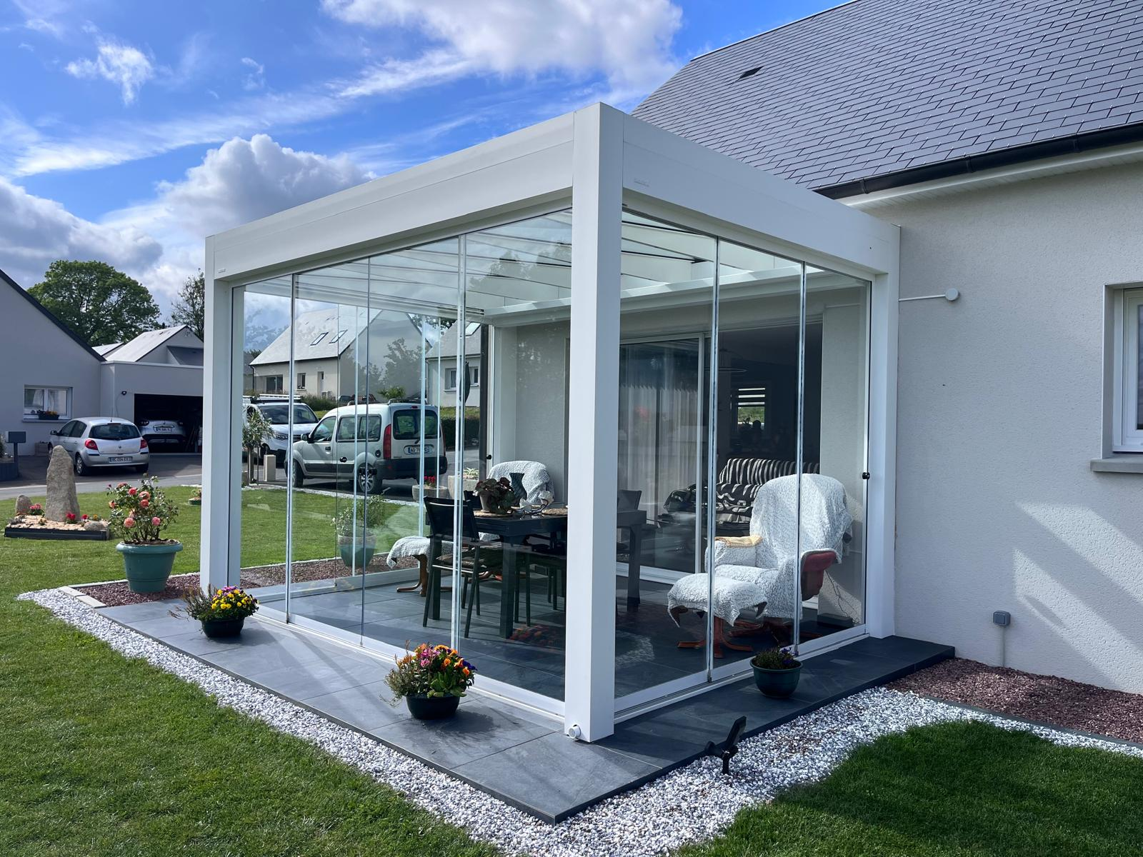 Pergola blanche à toiture et parois vitrées, coin repas intérieur, terrasse dalles grises