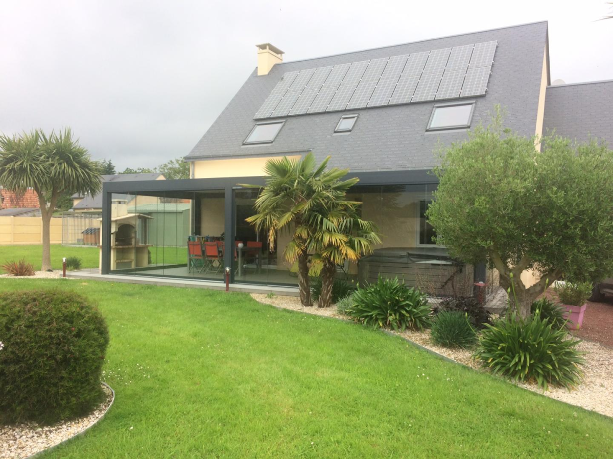 Veranda vitree anthracite devant une maison crème avec panneaux solaires en toiture