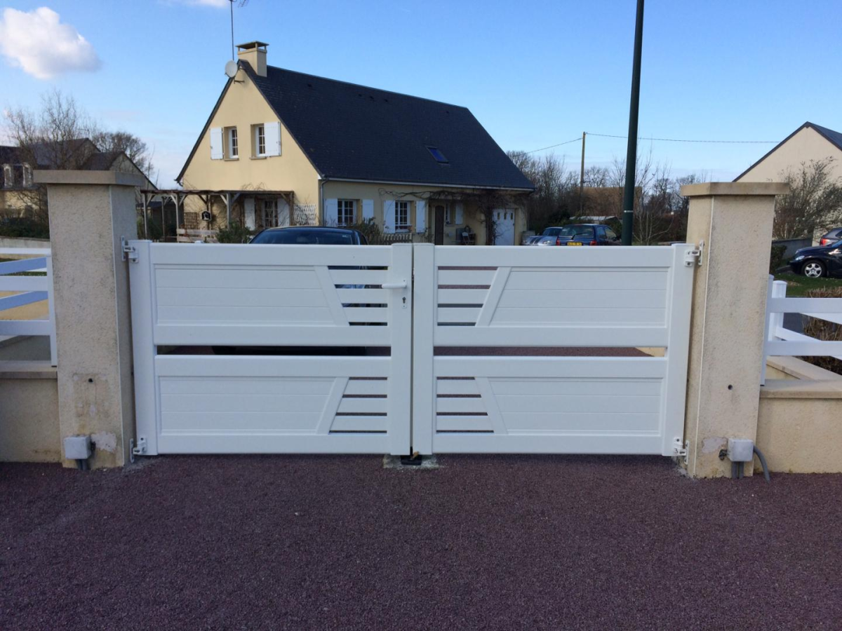 Portail battant blanc motifs ajourés horizontaux entre piliers crème sur gravier rouge